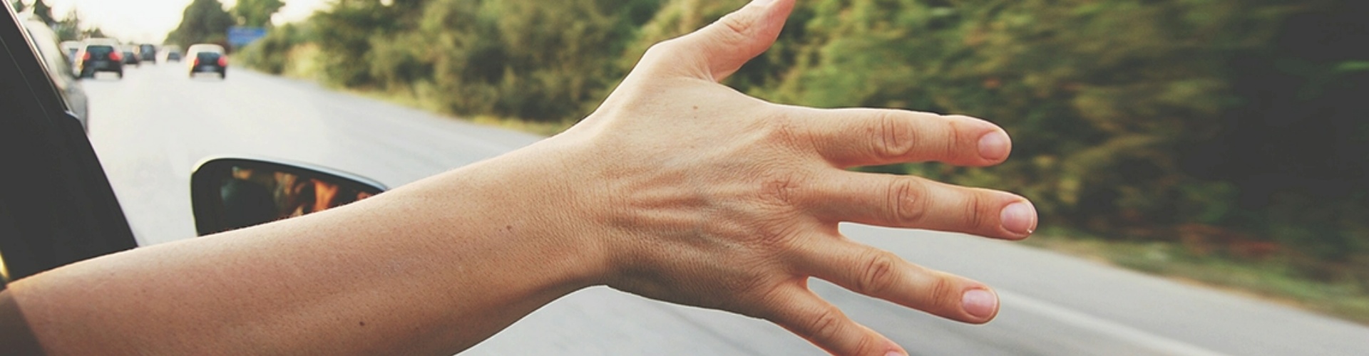 A person driving along a road with their hand out the window.