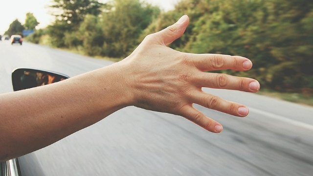 A person driving along a road with their hand out the window.