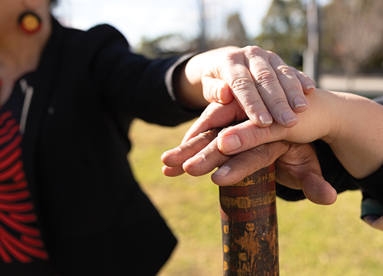 Hands stacked on a wooden stick with Aboriginal markings