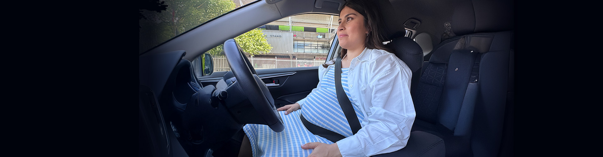 A pregnant woman in the drivers seat of a car wearing a seatbelt