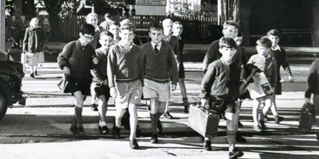 historic black and white picture of children using a school crossing equipped with a traffic light 