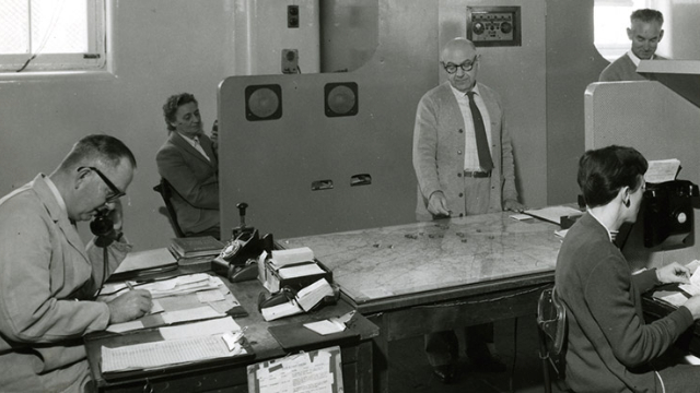 black and white picture of six employees using old-fashioned phones and a map to manage assistance calls and nrma patrol deployments
