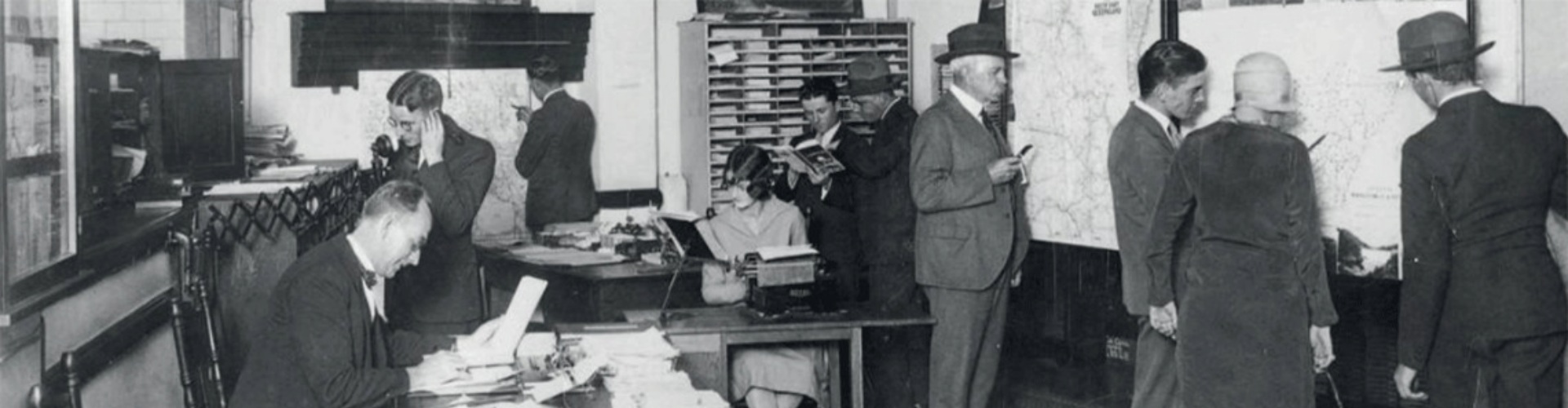 Cecil Albert Gregory NRMA offices, Sydney black and white photograph of the NRMA office with Cecil Gregory seated at a desk writing and other employees on the telephone, typing or looking at large wall maps
