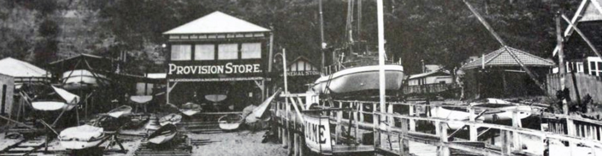 nrma-centenary-then-and-now-fantasea-cruising-1920x500 A black and white photo of the Palm beach wharf, where kayaks and small boats surround buildings, including a general store.