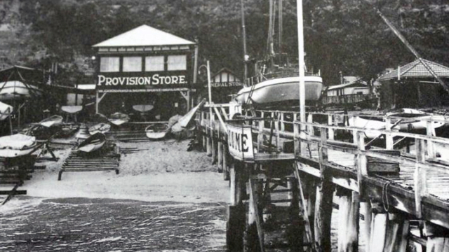 A black and white photo of the Palm beach wharf, where kayaks and small boats surround buildings, including a general store.
