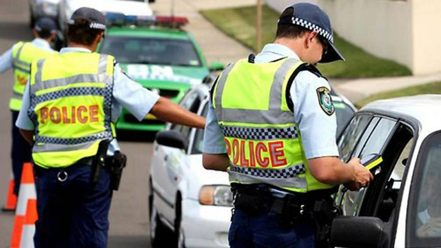 Police officers stopping a line of cars for random breath testing on a sunny day.