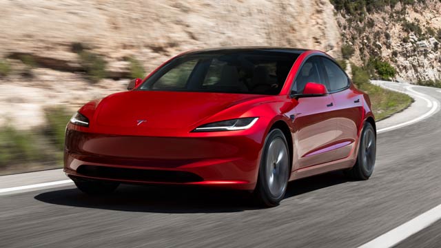 A red Model 3 driving in front of a sandstone wall
