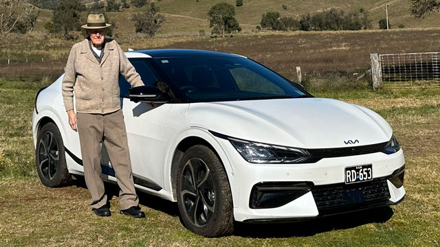 An aged man standing next to a white Kia EV6 electric car