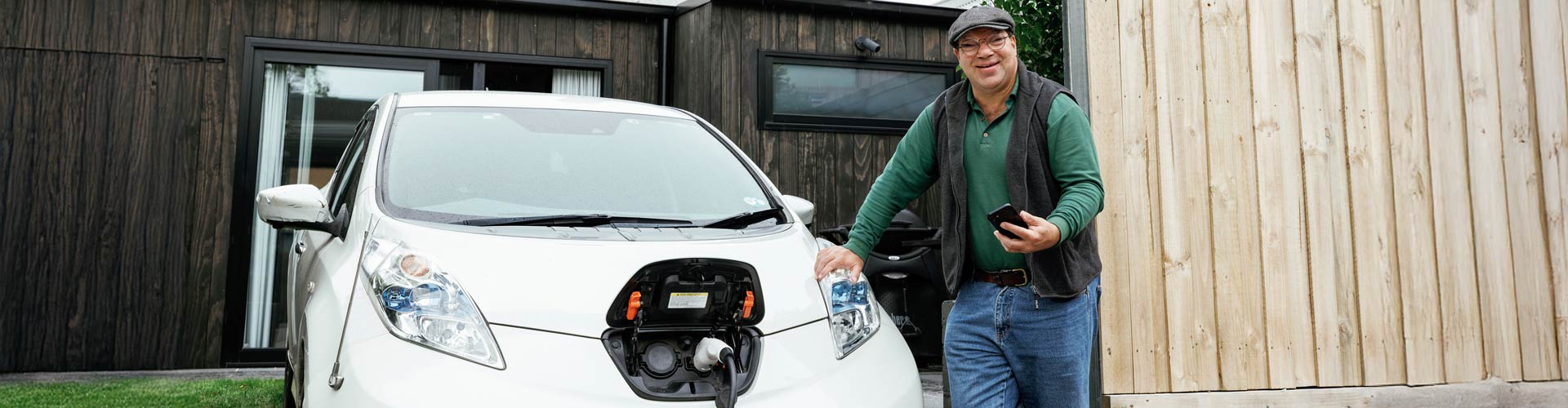 A man standing next to a white plugged-in Nissan Leaf