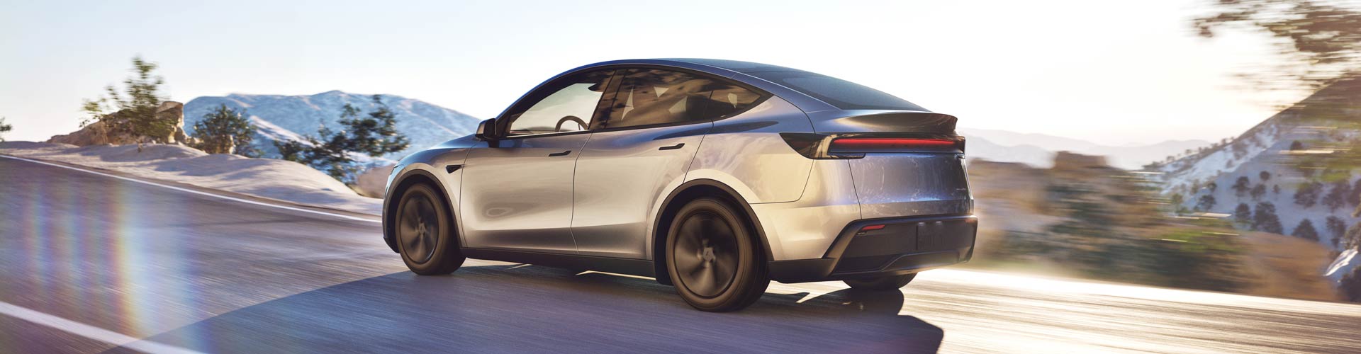 Silver Tesla Model Y seen from rear angle driving on mountain road