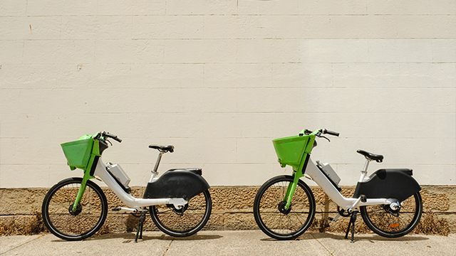 Two green e-bikes against a wall