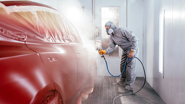 A man wearing a mask spraypainting a car red