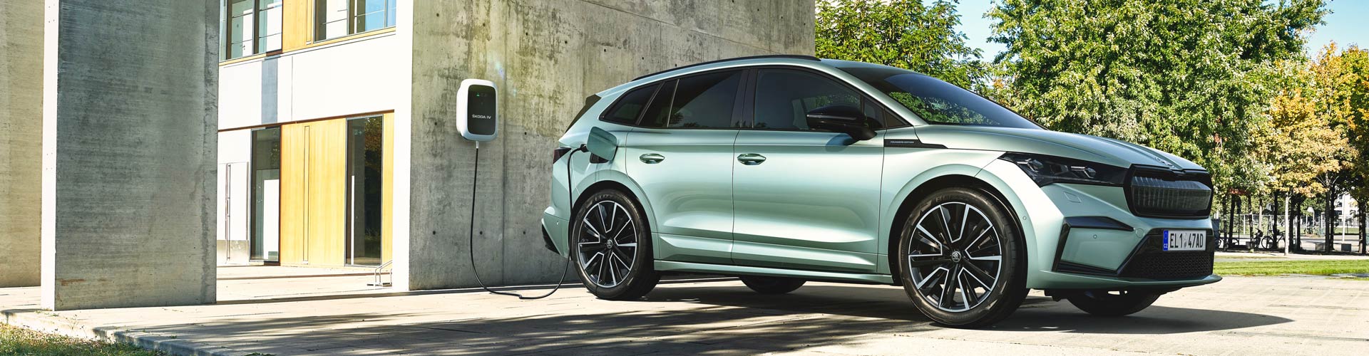 A silver green Skoda EV charges on the side of an apartment building