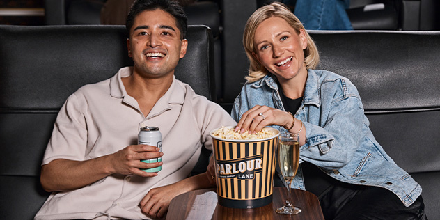 A man and a woman share a bucket  of popcorn in gold class