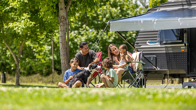 A family picnicking on the grass in front of a campervan