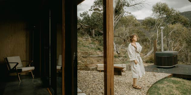 A woman stands outside in her dressing gown enjoying a bush scene