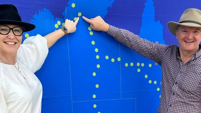 A women and man standing in front of a big blue map and pointing to it.
