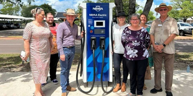 A group of people standing outdoors on either side of a blue NRMA-branded fast charger.