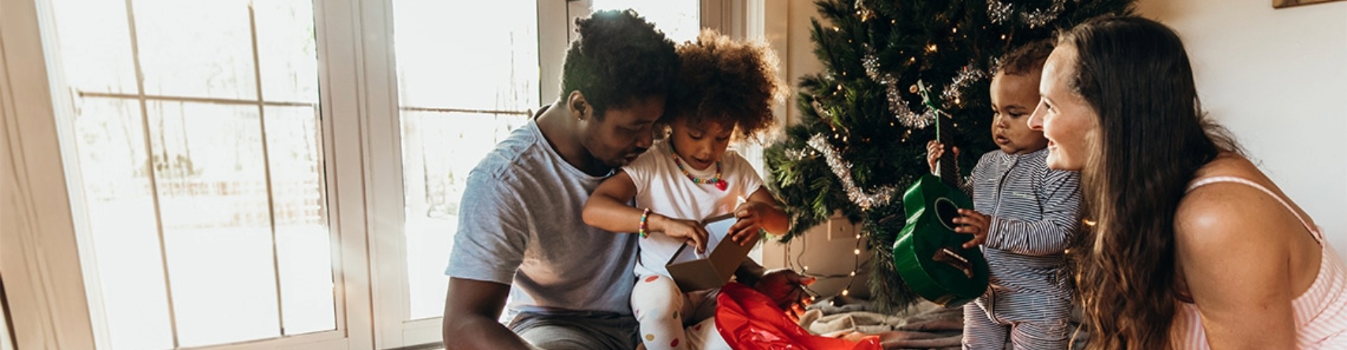 Family opening Christmas gifts family with young children opening gifts next to a christmas tree