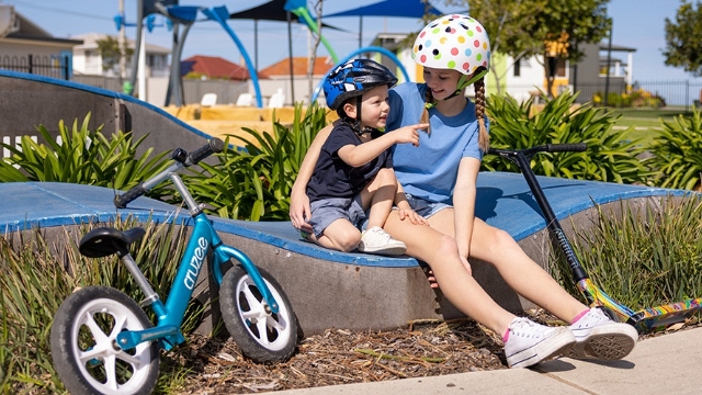 small boy and teen girl with cycling helmets on sit on wave shaped skate ramp in play park