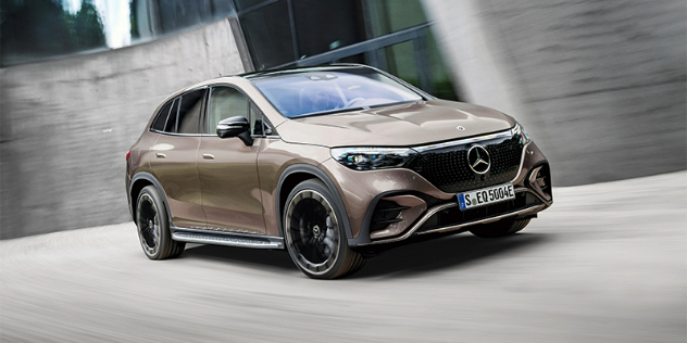 Front-angled view of a gold Mercedes Benz EQE suv parked in front of big cream coloured walls.