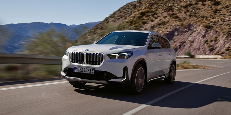 A white 2024 BMW iX1 eDrive20 drives along a mountainous country road