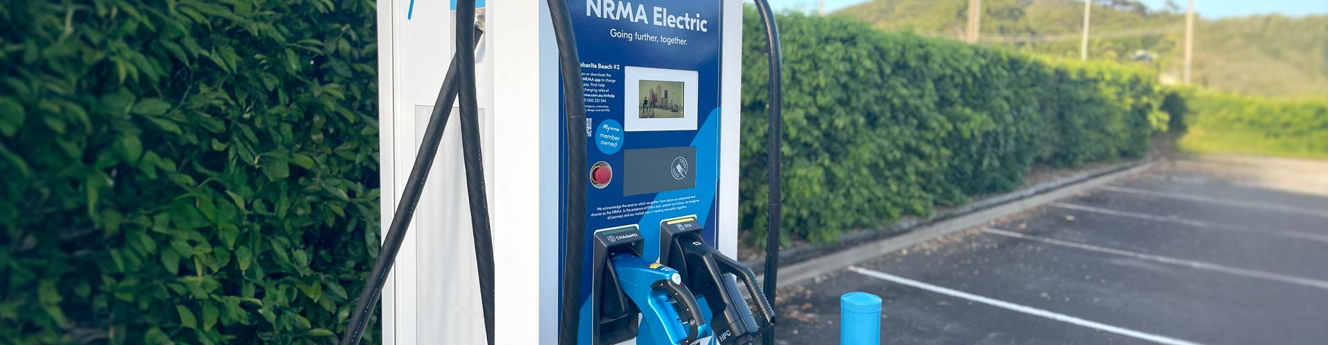 Blue EV charger in front of green hedge