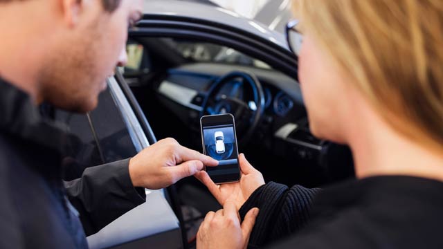 A man and woman look at a car app outside the vehicle