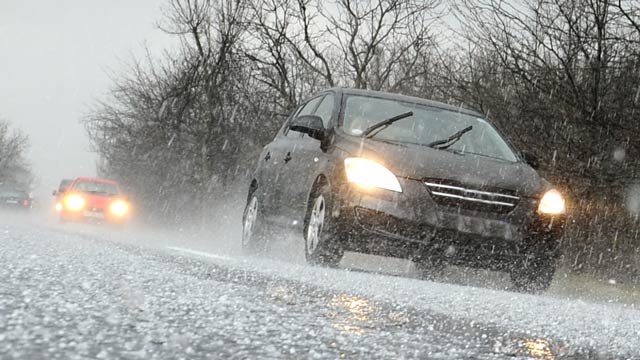 A black car driving in light hail on a wintry road