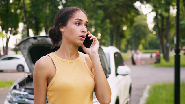 Young woman in orange singlet on phone in front of her white car