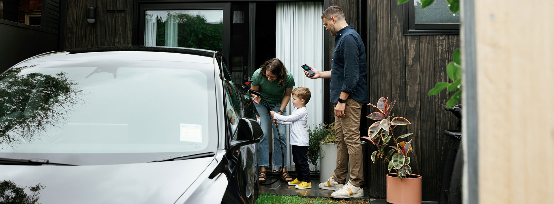 A young boy plugs in an EV while mum and dad watch in front of a house