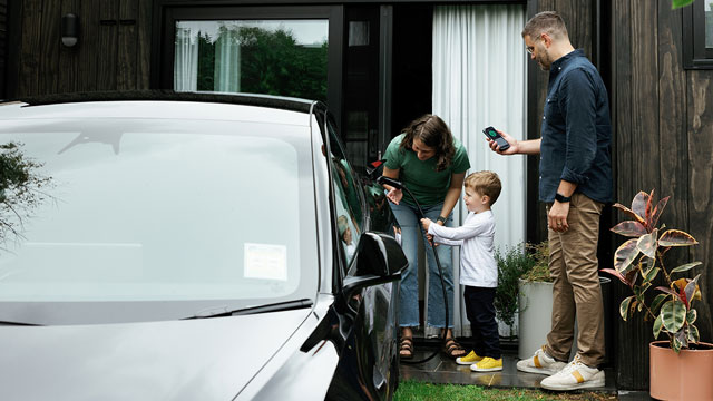 A young boy plugs in an EV while mum and dad watch in front of a house