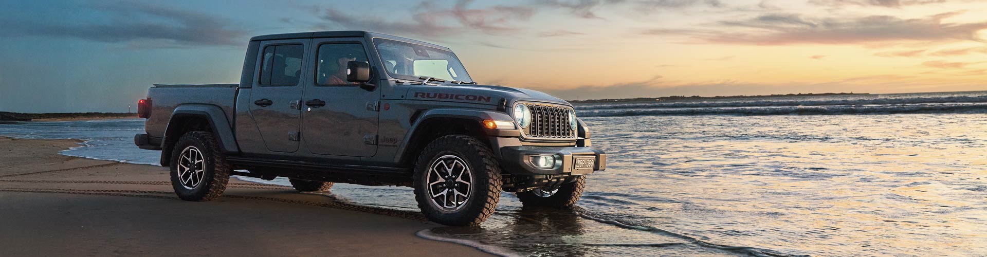 Jeep Wrangler parked on beach with tyres in water