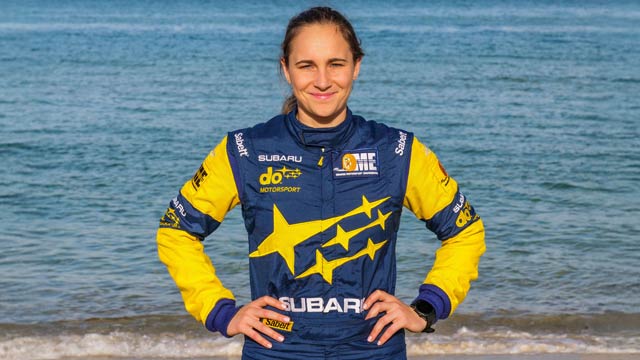 Molly Taylor standing in blue and yellow jacket in front of ocean