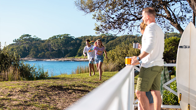 A person stands at a deck as children run past by the beach