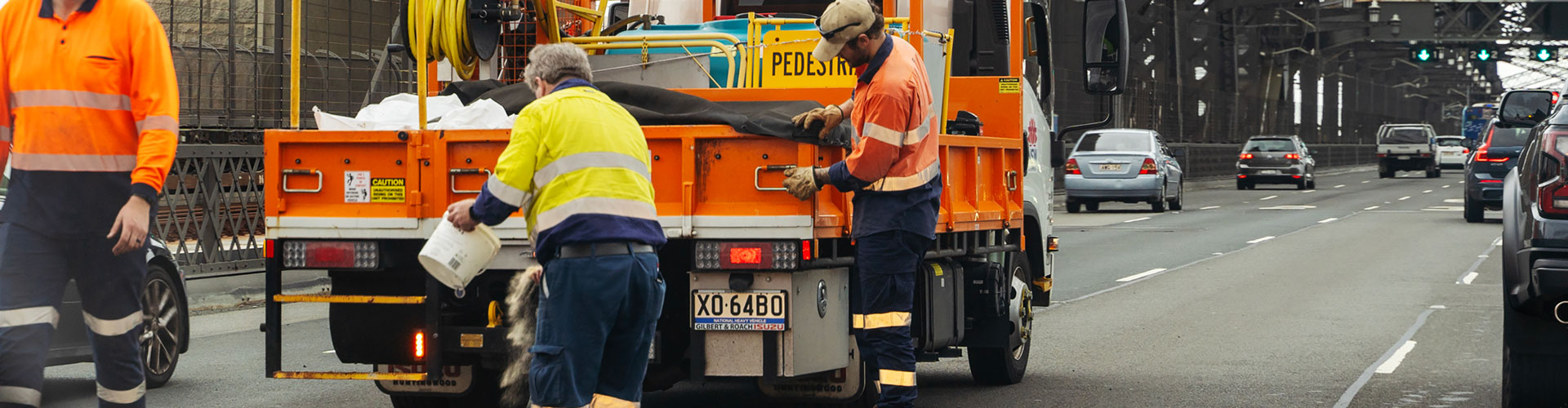 Workers stand near orange truck fixing road on Sydney Harbour Bridge