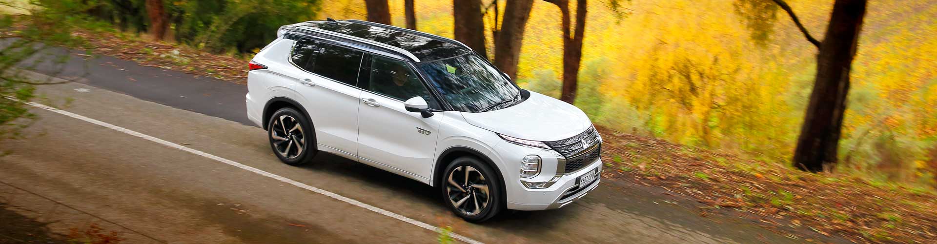 A white 2022 Mitsubishi Outlander Plug-In Hybrid Electric Vehicle driving on a country road
