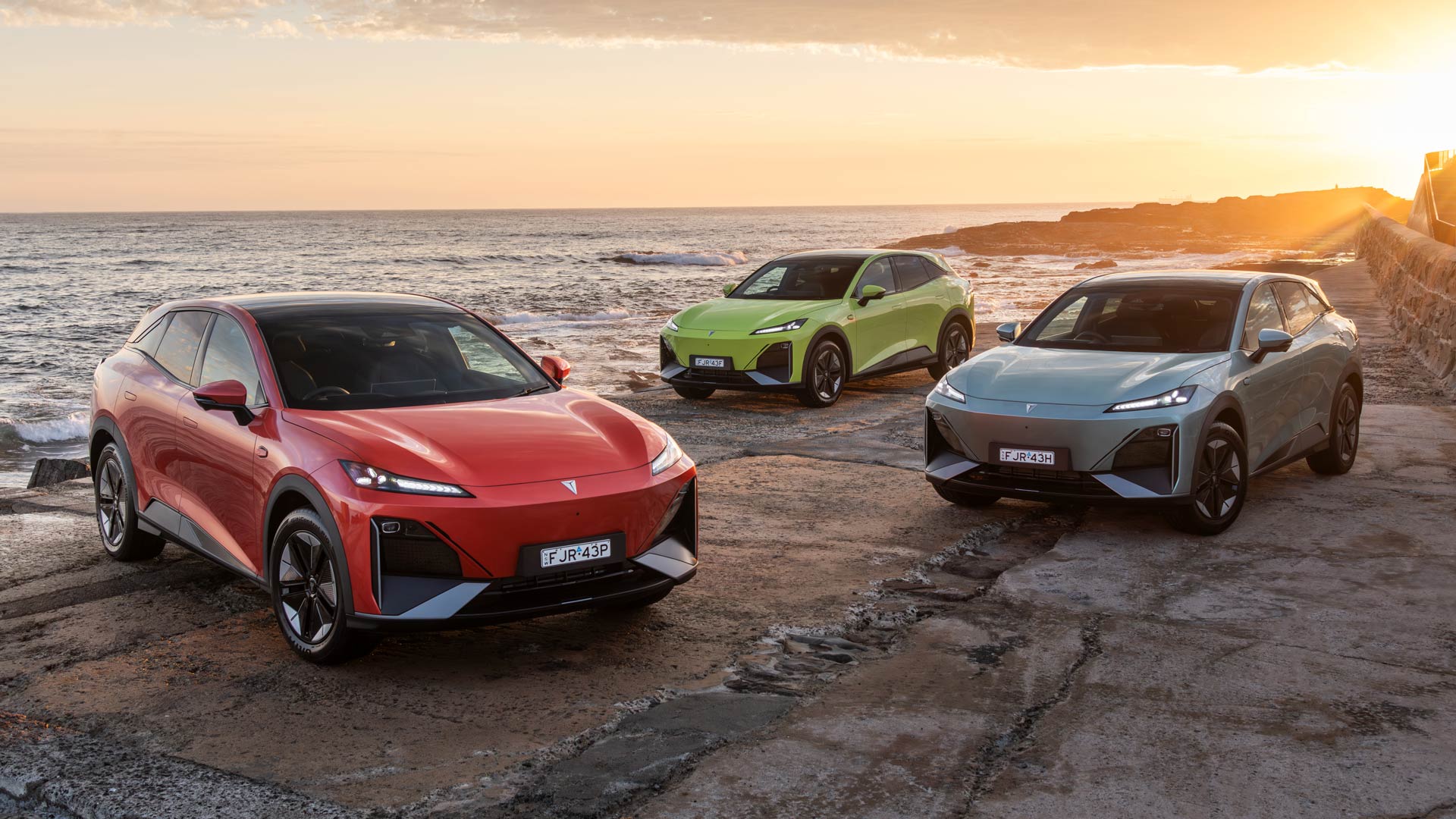 Three Deepal S07s in yellow, red and silver parked on a shorefront with sunset ocean scene behind