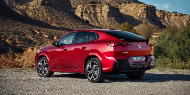 A red 2024 BMW iX2 parked against a rocky mountain range