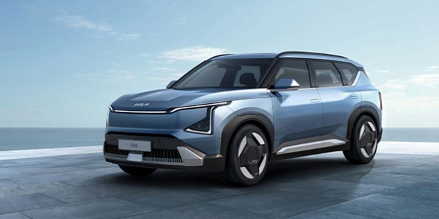 A metallic blue 2024 Kia EV5 sits parked on a futuristic platform beside the sea