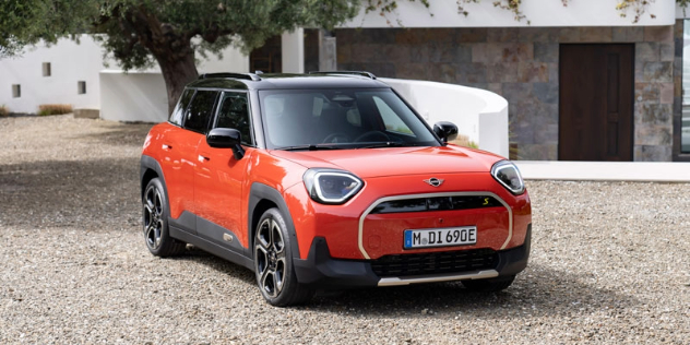 An orange 2024 Mini Aceman parked on a gravel path beside a country estate