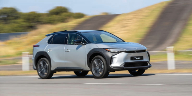 A silver 2024 Toyota bZ4X drives along a country road