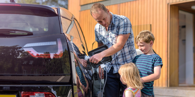 Children watching their dad plug in the family electric vehicle