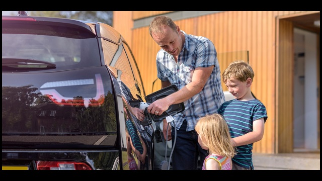 A person plugs their EV in to charge in their driveway