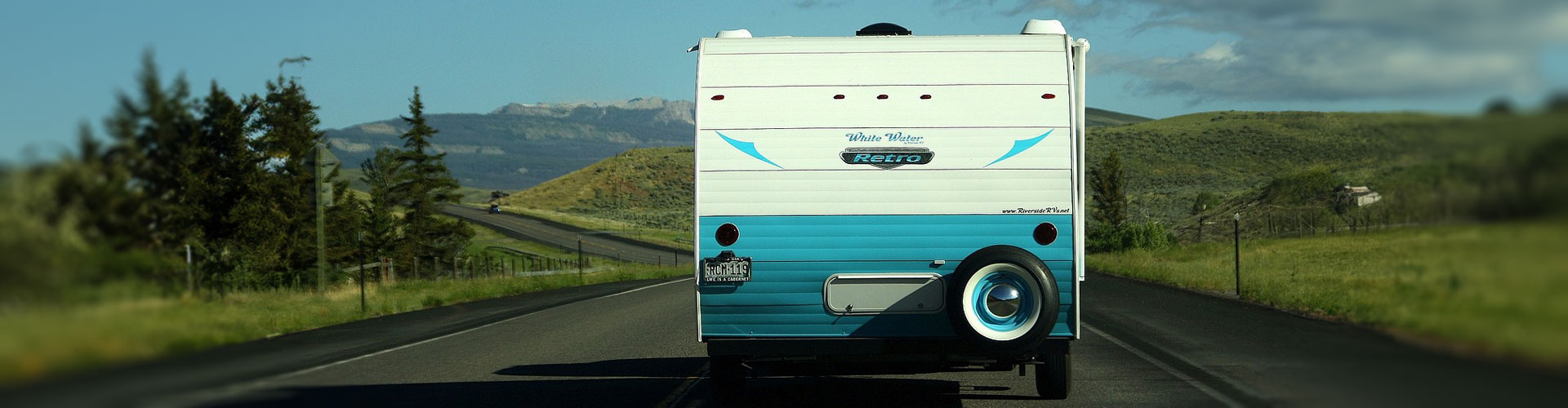 Rear view of blue and white caravan driving on a road towards mountains