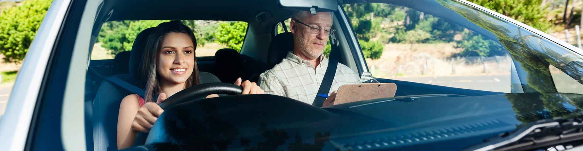 A young woman sits in the driver seat of a car next to a driving instructor