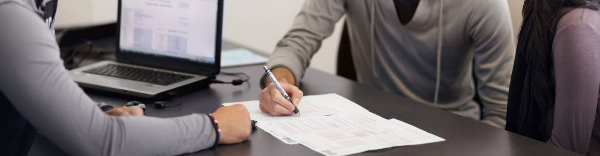 Cropped shot of a couple signing a contract at a desk across from a man with a laptop