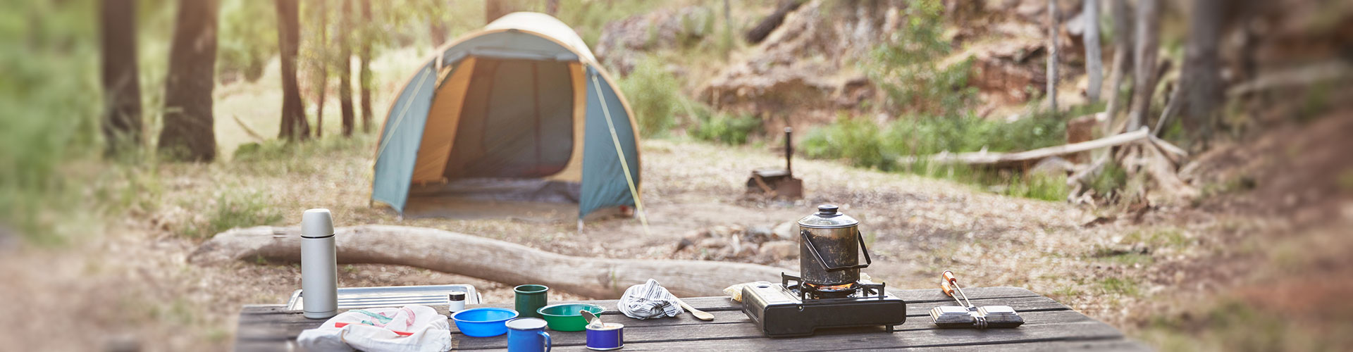 Image of campsite with tea making items on wooden table in foreground