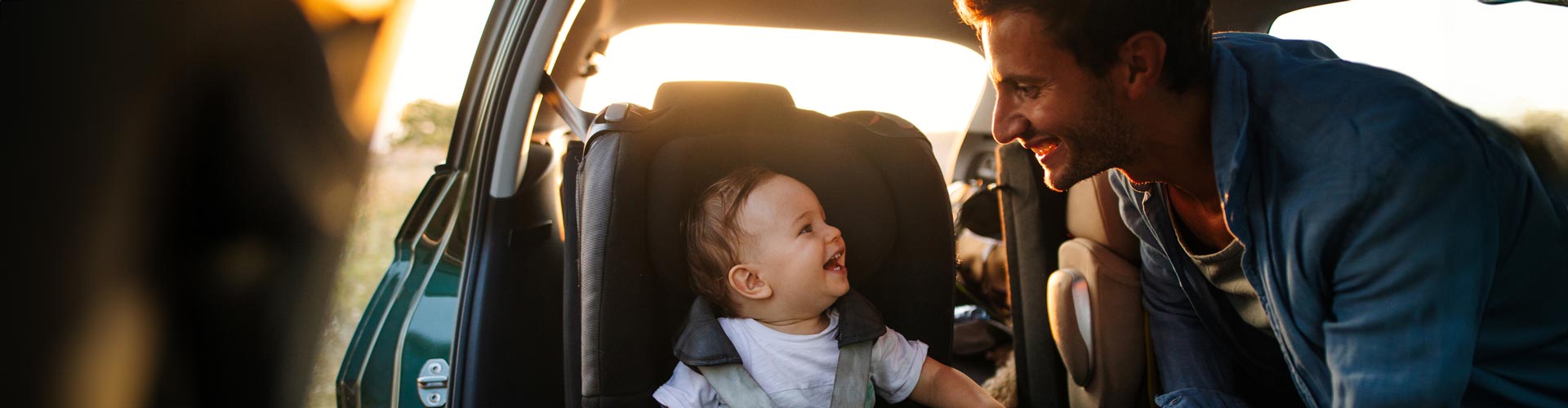 A father smiles while looking at his baby in the car seat with the doors open