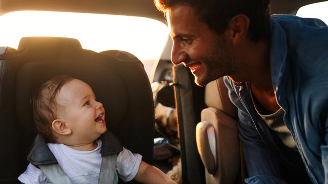 A father smiles while looking at his baby in the car seat with the doors open